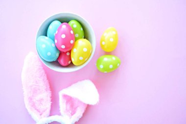 Üzerinde tavşan kulakları olan bir saç bandı pembe bir arka plan üzerinde, yanında beyaz noktalı Paskalya yumurtaları dolu bir eşarp - pastel renkleri ile Paskalya için renkler ile kavram -