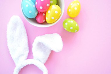 Üzerinde tavşan kulakları olan bir saç bandı pembe bir arka plan üzerinde, yanında beyaz noktalı Paskalya yumurtaları dolu bir eşarp - pastel renkleri ile Paskalya için renkler ile kavram -