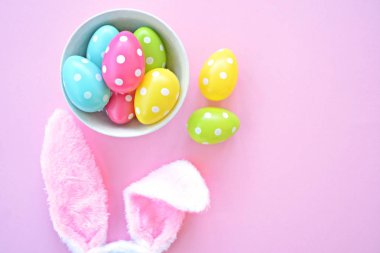 Üzerinde tavşan kulakları olan bir saç bandı pembe bir arka plan üzerinde, yanında beyaz noktalı Paskalya yumurtaları dolu bir eşarp - pastel renkleri ile Paskalya için renkler ile kavram -