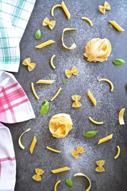 Erişte kelimesi unla kirlenmiş bir alanda, koyu mermer bir yüzeyde penne, farfalle ve fesleğen yaprakları gibi çeşitli makarnaçeşitleriyle birlikte yazılmıştır.