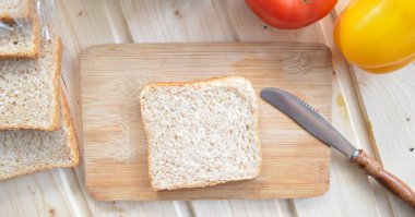 Kaba-taneli krem peyniri ve Cress ile bir kepekli tost bir bıçak yanında bir tahta tahta ve biber ve domates gibi sebze, yanı sıra Cress, salatalık ve havuç bir masada yatıyor