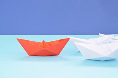 Kırmızı kendi kendine katlanmış kağıt tekne mavi bir yüzey üzerinde yatıyor, birçok beyaz tekneler izledi-kavramı liderlik sembolize