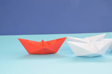 Kırmızı kendi kendine katlanmış kağıt tekne mavi bir yüzey üzerinde yatıyor, birçok beyaz tekneler izledi-kavramı liderlik sembolize