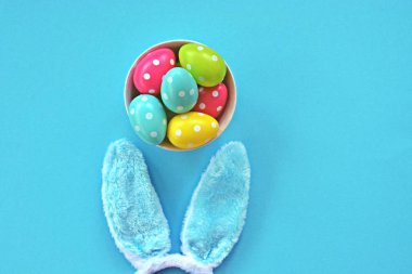 Mavi tavşan kulakları ile bir kafa bandı mavi bir yüzey üzerinde yatıyor, yanında onlara beyaz nokta ile renkli Paskalya yumurtaları - bir kafa bandı ve plastik yumurta ile Paskalya için kavram