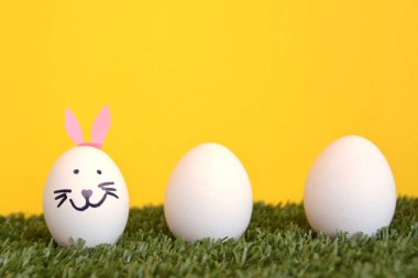 bir tavşan yüzü ile boyanmış ve tavşan kulakları yapıştırılmış yumurta metin veya diğer öğeler için alan ile ahşap bir arka plan önünde bir çim alan üzerinde yalan