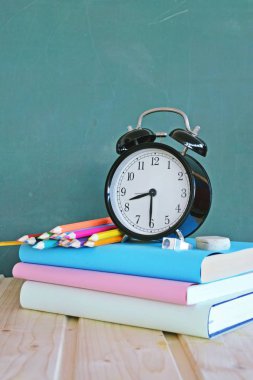 Bir çalar saat renkli kitaplar ve yeşil elma ile bir tahta önünde duruyor - ilköğretim okulunda okul ve zaman yönetimi konusunda metin veya diğer unsurlar için alan ile kavram