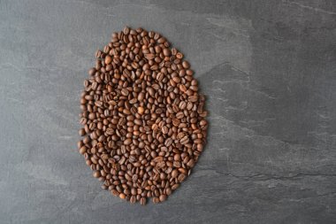 Koyu mermer yüzeyde taze kavrulmuş kahve çekirdeklerinden yapılmış bir kahve çekirdeği şekli - taze kahve keyfi için kavram 