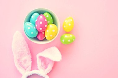 Üzerinde tavşan kulakları olan bir saç bandı pembe bir arka plan üzerinde, yanında beyaz noktalı Paskalya yumurtaları dolu bir eşarp - pastel renkleri ile Paskalya için renkler ile kavram -