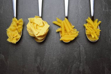 Erişte kelimesi unla kirlenmiş bir alanda, koyu mermer bir yüzeyde penne, farfalle ve fesleğen yaprakları gibi çeşitli makarnaçeşitleriyle birlikte yazılmıştır.