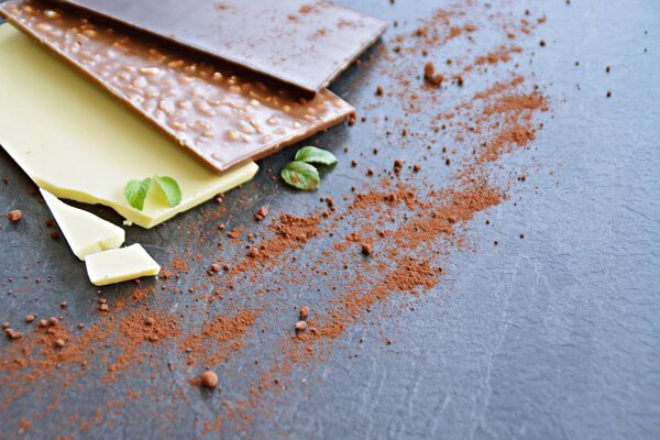 Три плитки темного шоколада, орехи и белый шоколад лежат на темной мраморной поверхности - шоколад на темной поверхности с местом для текста или других элементов
