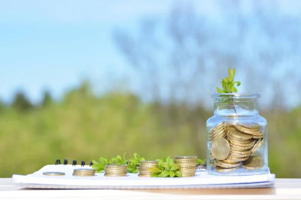 A jar full of savings stands on a space next to a purse of saved coins that pile up to form a tall tower - saving concept with room for text or other items