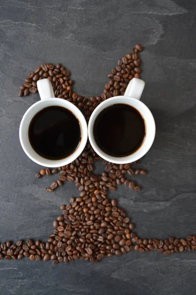 An Easter bunny made of freshly roasted coffee beans laid out with a cup of coffee - concept for fresh coffee enjoyment on easter and as easter gift in the form of coffee beans