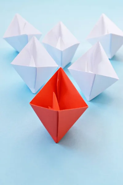 A red self-folded paper boat lies on a blue surface, followed by many white boats - concept symbolizing leadership