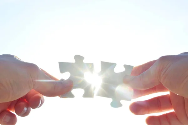 A person holds two puzzle pieces in his hand that fit together, in the background the sun shines and illuminates the parts from behind - concept for brainstorming in the professional environment