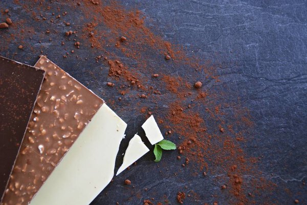 Три плитки темного шоколада, орехи и белый шоколад лежат на темной мраморной поверхности - шоколад на темной поверхности с местом для текста или других элементов
