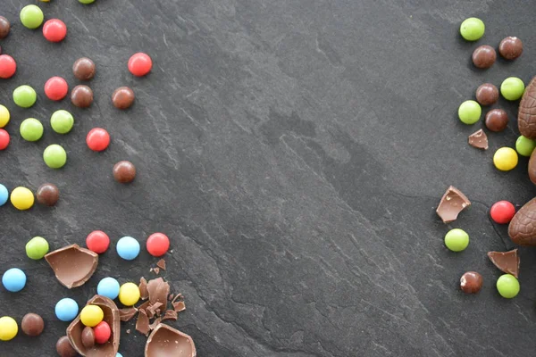 A chocolate easter bunny lies on a dark marble surface with colorful chocolate chips and a few chocolate eggs - concept with sweets for easter with room for text or other elements