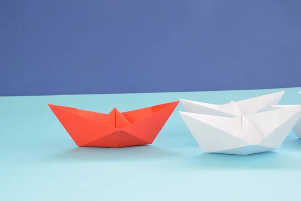 A red self-folded paper boat lies on a blue surface, followed by many white boats - concept symbolizing leadership