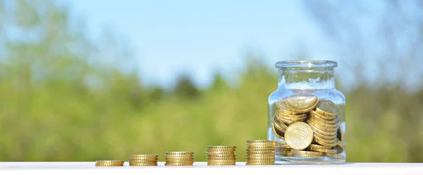 A jar full of savings stands on a space next to a purse of saved coins that pile up to form a tall tower - saving concept with room for text or other items