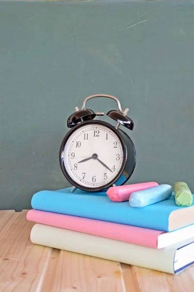 An alarm clock stands in front of a blackboard with colorful books and a green apple - concept with space for text or other elements on the subject of school and time management in elementary school