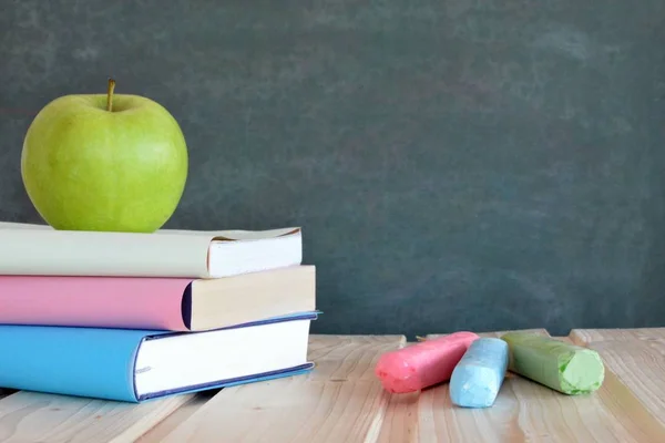 異なる色のカバーを持つ3冊の本は リンゴと黒板の前に木製の表面に横たわっている テキストや他の要素のための場所を持つ教育や学校のための概念 — ストック写真