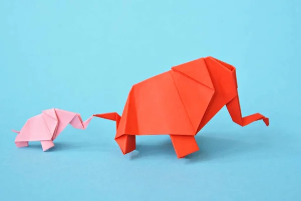 Two paper-folded elephants in pink and red stand on a blue background - concept with a little baby elephant and a mother elephant folded according to the origami technique