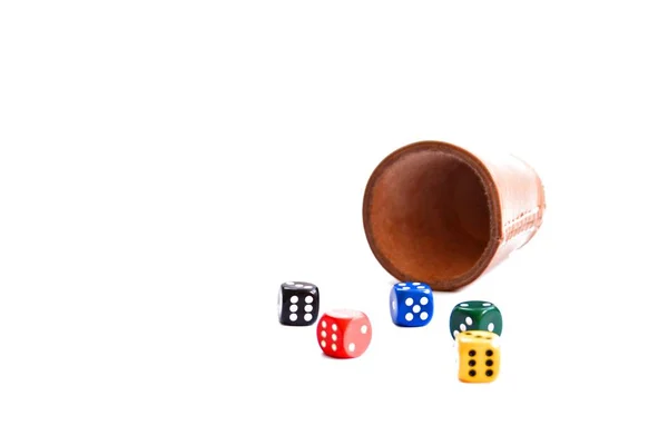 A dice cup stands with many different dice in different colors and game figures in the same colors on a white surface