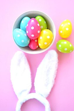 Üzerinde tavşan kulakları olan bir saç bandı pembe bir arka plan üzerinde, yanında beyaz noktalı Paskalya yumurtaları dolu bir eşarp - pastel renkleri ile Paskalya için renkler ile kavram -