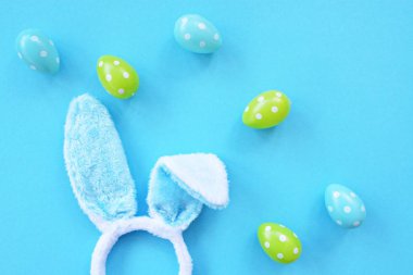 Mavi tavşan kulakları ile bir kafa bandı mavi bir yüzey üzerinde yatıyor, yanında onlara beyaz nokta ile renkli Paskalya yumurtaları - bir kafa bandı ve plastik yumurta ile Paskalya için kavram
