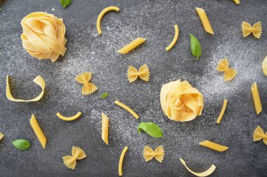 Erişte kelimesi unla kirlenmiş bir alanda, koyu mermer bir yüzeyde penne, farfalle ve fesleğen yaprakları gibi çeşitli makarnaçeşitleriyle birlikte yazılmıştır.