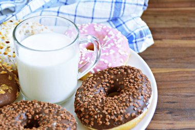 Bir plaka üzerinde lezzetli taze Donuts-ahşap bir yüzey üzerinde Sprinkles ve fındık ile farklı Glasuer var farklı Donuts, bir plaka