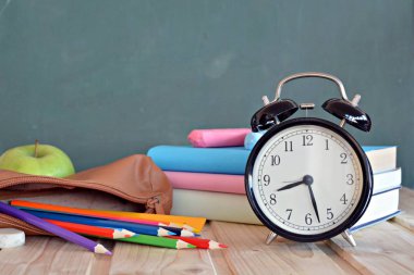 Bir çalar saat renkli kitaplar ve yeşil elma ile bir tahta önünde duruyor - ilköğretim okulunda okul ve zaman yönetimi konusunda metin veya diğer unsurlar için alan ile kavram