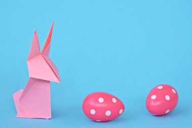 Pastel kağıt tan katlanmış pembe bir origami tavşan ı da beyaz nokta ile Paskalya yumurtası olan mavi bir taban üzerinde duruyor - origami ve metin veya Paskalya için diğer unsurlar için alan kavramı 