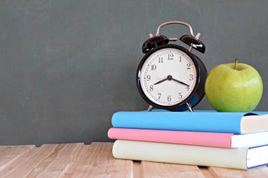 Bir çalar saat renkli kitaplar ve yeşil elma ile bir tahta önünde duruyor - ilköğretim okulunda okul ve zaman yönetimi konusunda metin veya diğer unsurlar için alan ile kavram