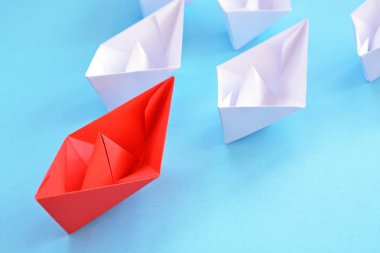 Kırmızı kendi kendine katlanmış kağıt tekne mavi bir yüzey üzerinde yatıyor, birçok beyaz tekneler izledi-kavramı liderlik sembolize