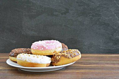 Bir plaka üzerinde lezzetli taze Donuts-ahşap bir yüzey üzerinde Sprinkles ve fındık ile farklı Glasuer var farklı Donuts, bir plaka