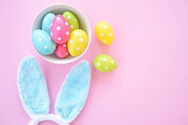 Üzerinde tavşan kulakları olan bir saç bandı pembe bir arka plan üzerinde, yanında beyaz noktalı Paskalya yumurtaları dolu bir eşarp - pastel renkleri ile Paskalya için renkler ile kavram -