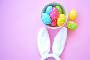Üzerinde tavşan kulakları olan bir saç bandı pembe bir arka plan üzerinde, yanında beyaz noktalı Paskalya yumurtaları dolu bir eşarp - pastel renkleri ile Paskalya için renkler ile kavram -