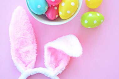 Üzerinde tavşan kulakları olan bir saç bandı pembe bir arka plan üzerinde, yanında beyaz noktalı Paskalya yumurtaları dolu bir eşarp - pastel renkleri ile Paskalya için renkler ile kavram -