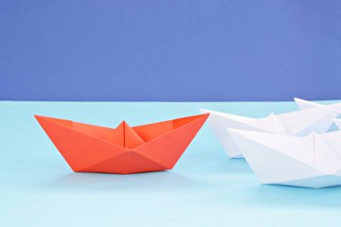 Kırmızı kendi kendine katlanmış kağıt tekne mavi bir yüzey üzerinde yatıyor, birçok beyaz tekneler izledi-kavramı liderlik sembolize