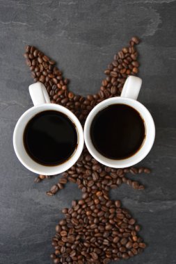 Bir Paskalya tavşanı taze kavrulmuş kahve çekirdekleri bir fincan kahve ile ortaya koydu - paskalya taze kahve keyfi için kavram ve kahve çekirdekleri şeklinde paskalya hediyesi olarak