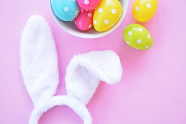 Üzerinde tavşan kulakları olan bir saç bandı pembe bir arka plan üzerinde, yanında beyaz noktalı Paskalya yumurtaları dolu bir eşarp - pastel renkleri ile Paskalya için renkler ile kavram -