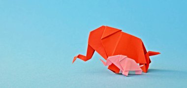 Küçük ve büyük bir origami fil iki fil gibi görünen bir ayna parçası önünde tek renkli bir yüzey üzerinde kırmızı ve pembe kağıt standı katlanmış bir su deliğinin önünde duruyor 