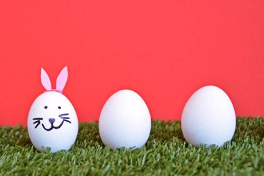 bir tavşan yüzü ile boyanmış ve tavşan kulakları yapıştırılmış yumurta metin veya diğer öğeler için alan ile ahşap bir arka plan önünde bir çim alan üzerinde yalan