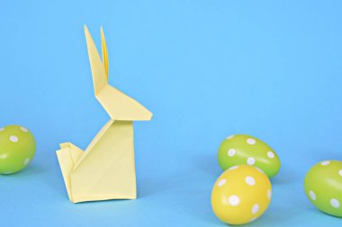 Pastel kağıt tan katlanmış pembe bir origami tavşan ı da beyaz nokta ile Paskalya yumurtası olan mavi bir taban üzerinde duruyor - origami ve metin veya Paskalya için diğer unsurlar için alan kavramı 