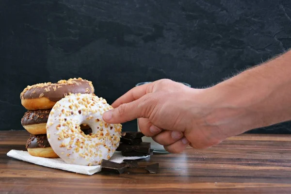 glazed donut with brittle splinters and other chocolate donuts lie on a dark wooden surface against a dark background and a glass of milk - concept for sweet donuts