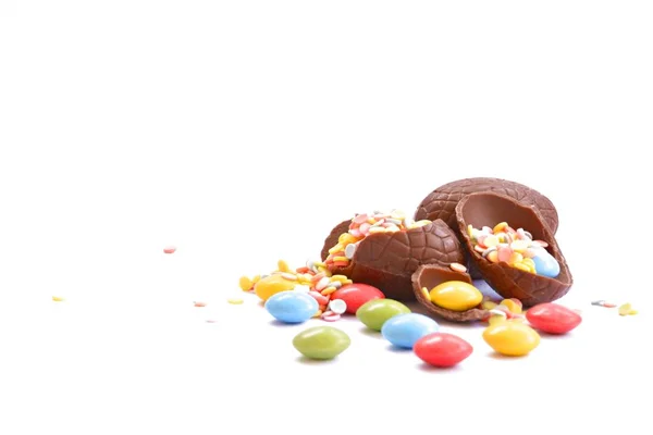 巧克力复活节彩蛋的碎片躺在白色表面上 里面装满了五颜六色的巧克力和纸屑 复活节小吃的概念 — 图库照片