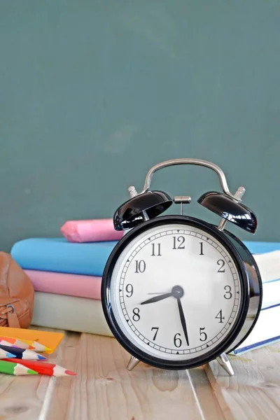 An alarm clock stands in front of a blackboard with colorful books and a green apple - concept with space for text or other elements on the subject of school and time management in elementary school