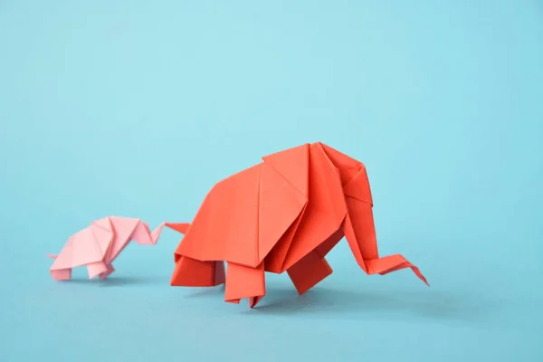 Two paper-folded elephants in pink and red stand on a blue background - concept with a little baby elephant and a mother elephant folded according to the origami technique