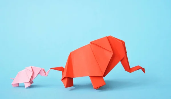 Two paper-folded elephants in pink and red stand on a blue background - concept with a little baby elephant and a mother elephant folded according to the origami technique