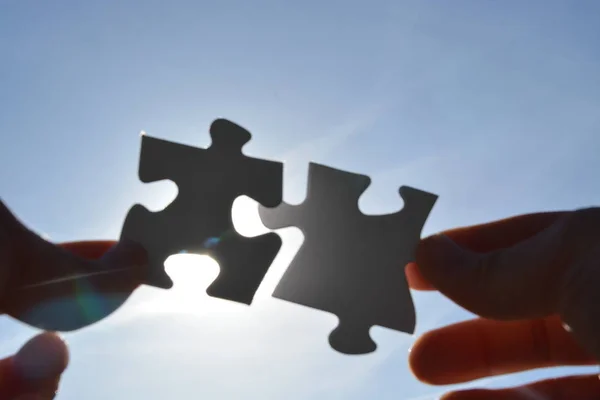 A person holds two puzzle pieces in his hand that fit together, in the background the sun shines and illuminates the parts from behind - concept for brainstorming in the professional environment